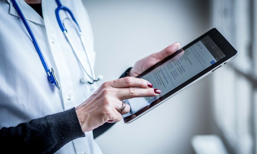 Osoba w białym fartuchu medycznym używa tabletu, przyglądając się ekranowi.