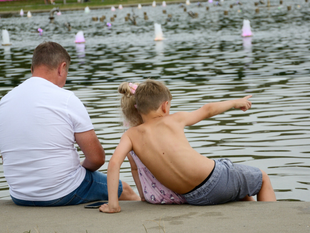 Mężczyzna, dziewczynka i chłopiec siedzą nad fontanną, chłopiec wskazuje w kierunku wody.