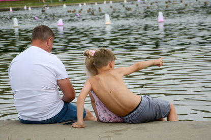 Mężczyzna, dziewczynka i chłopiec siedzą nad fontanną, chłopiec wskazuje w kierunku wody.