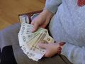Na zdjęciu widoczne ręce trzymające banknoty w różnych nominałach oraz portfel.