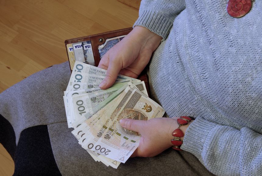 Na zdjęciu widoczne ręce trzymające banknoty w różnych nominałach oraz portfel.