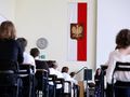 Sala z uczestnikami, w tle flaga Polski z godłem. Nauczycielka z przodu.