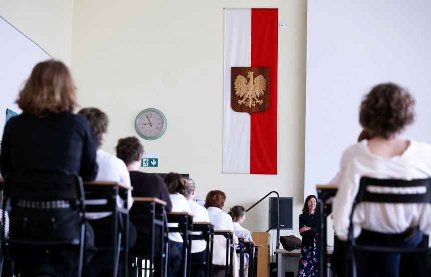 Sala z uczestnikami, w tle flaga Polski z godłem. Nauczycielka z przodu.