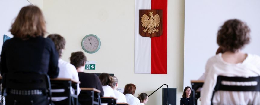 Sala z uczestnikami, w tle flaga Polski z godłem. Nauczycielka z przodu.