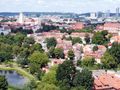 Widok na miasto z zielonymi drzewami i czerwonymi dachami, w tle nowoczesne budynki.