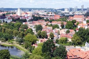 Widok na miasto z zielonymi drzewami i czerwonymi dachami, w tle nowoczesne budynki.