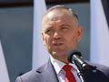 Mężczyzna w garniturze przemawia do mikrofonu, za nim widoczne flagi.
