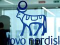 Logo firmy Novo Nordisk z niebieską krową i okręgiem na tle przeszklonej ściany.