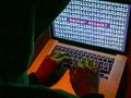 Osoba w kapuście siedzi przy laptopie, na którym wyświetla się komunikat 