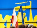 Dwa flagi: biało-czerwona Polski i niebiesko-żółta Ukrainy, w tle kolorowy napis.