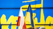 Dwa flagi: biało-czerwona Polski i niebiesko-żółta Ukrainy, w tle kolorowy napis.