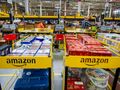 Magazyn Amazon z regałami pełnymi towarów, pracownicy przy pakowaniu zamówień.