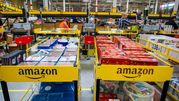 Magazyn Amazon z regałami pełnymi towarów, pracownicy przy pakowaniu zamówień.