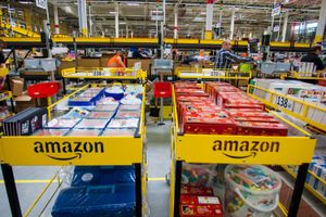 Magazyn Amazon z regałami pełnymi towarów, pracownicy przy pakowaniu zamówień.