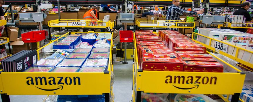 Magazyn Amazon z regałami pełnymi towarów, pracownicy przy pakowaniu zamówień.