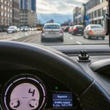 Widok z wnętrza samochodu, kierownica i ekran nawigacji, ruch uliczny w tle.