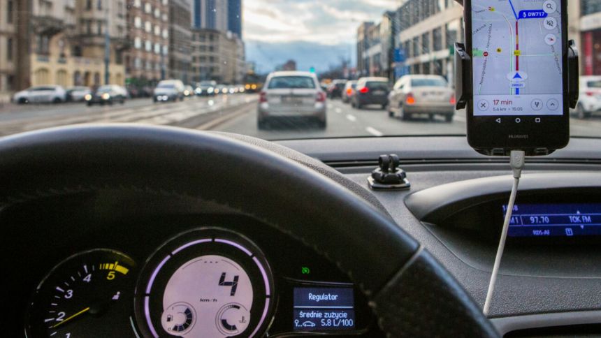 Widok z wnętrza samochodu, kierownica i ekran nawigacji, ruch uliczny w tle.