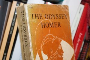 Okładka książki „The Odyssey” Homera na tle innych książek na półce.