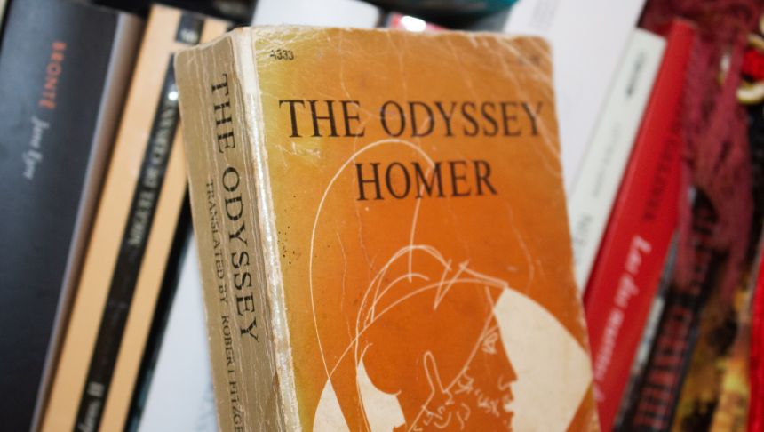 Okładka książki „The Odyssey” Homera na tle innych książek na półce.