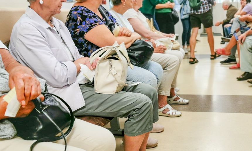 Opis ALT: Grupa osób siedzących na ławkach w przychodni, czekają na wizytę lekarską.