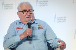 Lech Wałęsa w niebieskiej koszuli z wizerunkiem Matki Boskiej, trzyma mikrofon i mówi.
