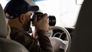 Mężczyzna trzymający aparat fotograficzny w samochodzie, widoczny z tyłu.