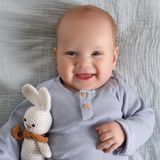 Uśmiechnięty niemowlak w niebieskiej koszulce trzyma pluszowego białego królika na niebieskim tle.