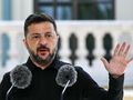 Mężczyzna w czarnym ubraniu, mówi przy mikrofonach, podnosząc dłoń w geście.