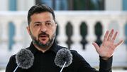 Mężczyzna w czarnym ubraniu, mówi przy mikrofonach, podnosząc dłoń w geście.