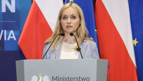 Na pierwszym planie kobieta z blond włosami stoi przy mównicy z logo ministerstwa.