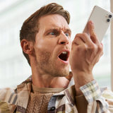 Mężczyzna w plaidowej koszuli, zdenerwowany, krzyczy w telefon. Tło jasne, okna za nim.