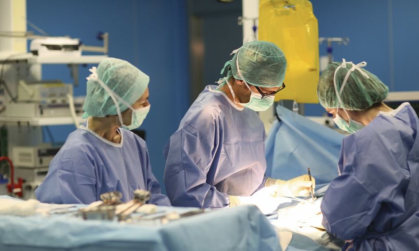 Grupa chirurgów w szpitalu skupiona na operacji, w maseczkach i odzieży ochronnej.
