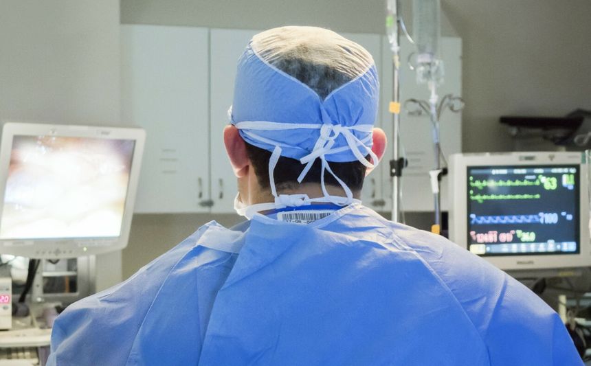 Na zdjęciu widoczny jest lekarz w niebieskim fartuchu i czepku, stojący przed monitorem w sali operacyjnej.