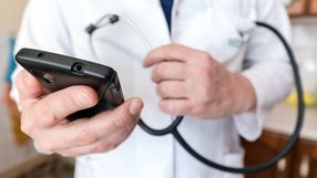 Mężczyzna w białym fartuchu trzyma telefon i stetoskop, przygotowując się do badania.
