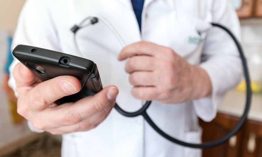 Mężczyzna w białym fartuchu trzyma telefon i stetoskop, przygotowując się do badania.