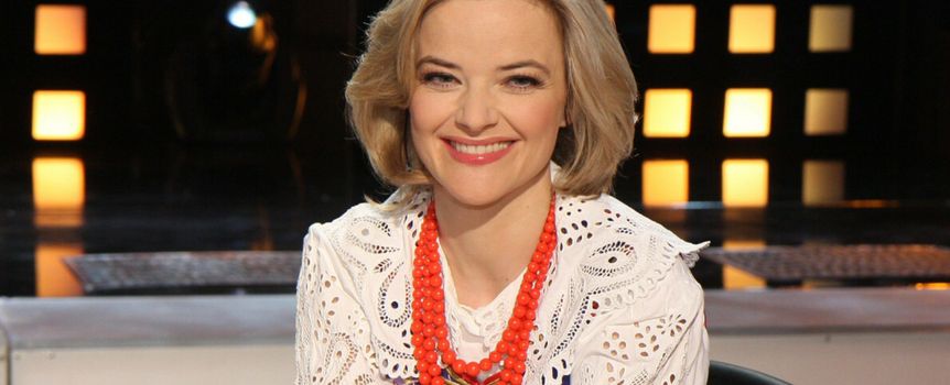 Kobieta z krótkimi, blond włosami, uśmiecha się i nosi kolorową biżuterię.