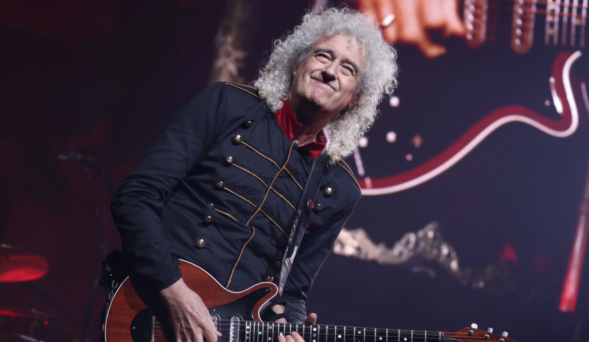 Brian May w czarnej kurtce i z czerwoną gitarą podczas koncertu