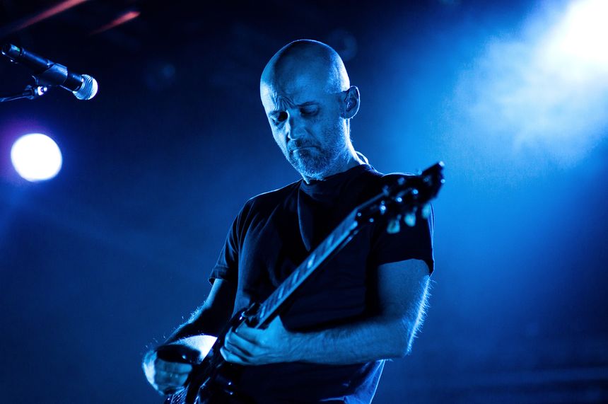 Mężczyzna gra na gitarze w niebieskim świetle sceny, skupiony na muzyce.