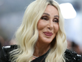 Zdjęcie uśmiechniętej kobiety z blond włosami w eleganckim stroju. Tło rozmyte.