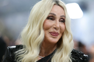 Zdjęcie uśmiechniętej kobiety z blond włosami w eleganckim stroju. Tło rozmyte.