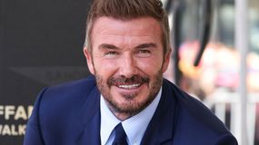 David Beckham w niebieskim garniturze, uśmiechnięty, z krótkimi, stylowymi włosami.