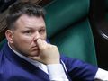 Mężczyzna w granatowym garniturze myśli, opierając dłoń na twarzy, siedząc w sejmie.