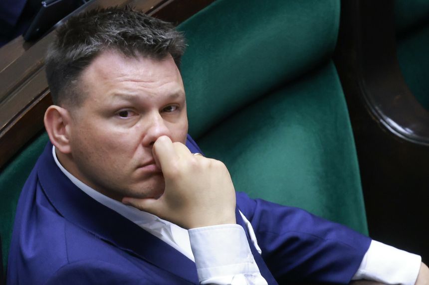 Mężczyzna w granatowym garniturze myśli, opierając dłoń na twarzy, siedząc w sejmie.