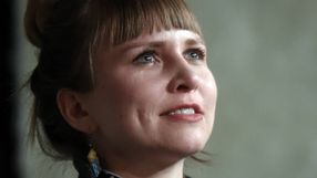 Kobieta z krótkimi włosami, patrzy w górę, uśmiechając się, w tle neutralny kolor.