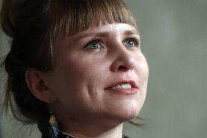 Kobieta z krótkimi włosami, patrzy w górę, uśmiechając się, w tle neutralny kolor.