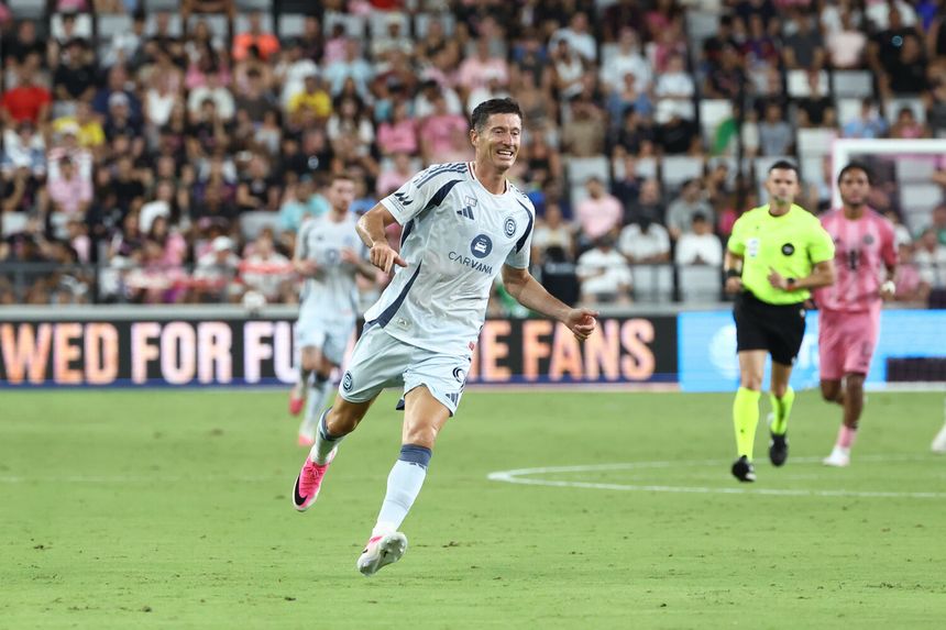 Robert Lewandowski w białej koszulce na boisku wypełnionym kibicami.