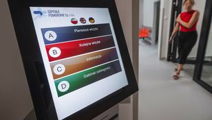 Wyświetlacz dotykowy z menu informacyjnym w nowoczesnym szpitalu. W tle przechodzi osoba.