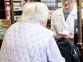 Kobieta w jasnej kurtce rozmawia z farmaceutką w aptece. W tle półki z lekami.