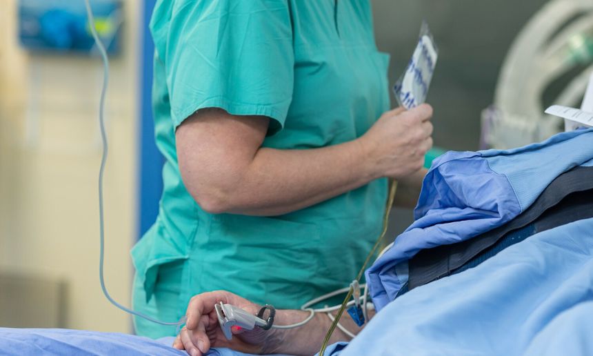 Osoba w zielonym fartuchu medycznym trzyma urządzenie, pacjent leży w niebieskim prześcieradle.