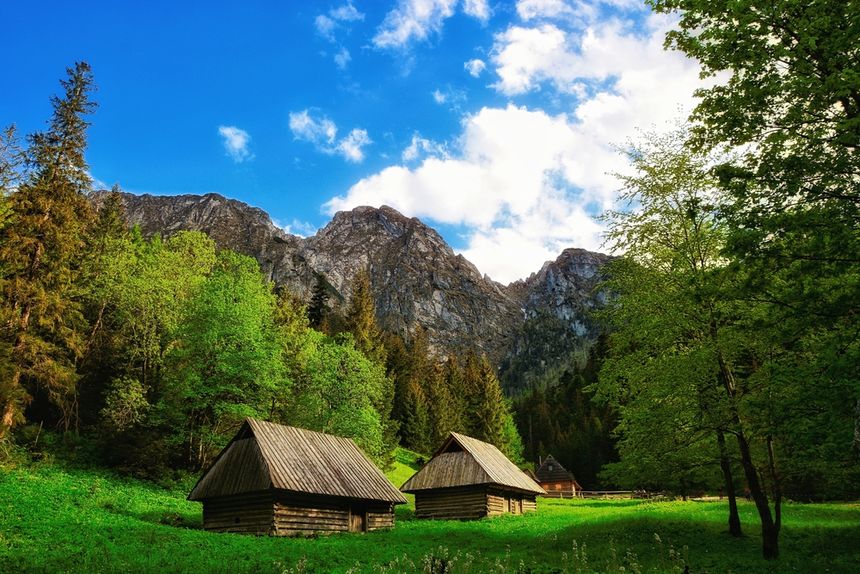 Widok gór z drewnianymi chatkami na tle zieleni i nieba z chmurami.